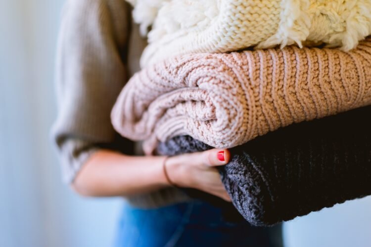 woman holding a stack of sweaters