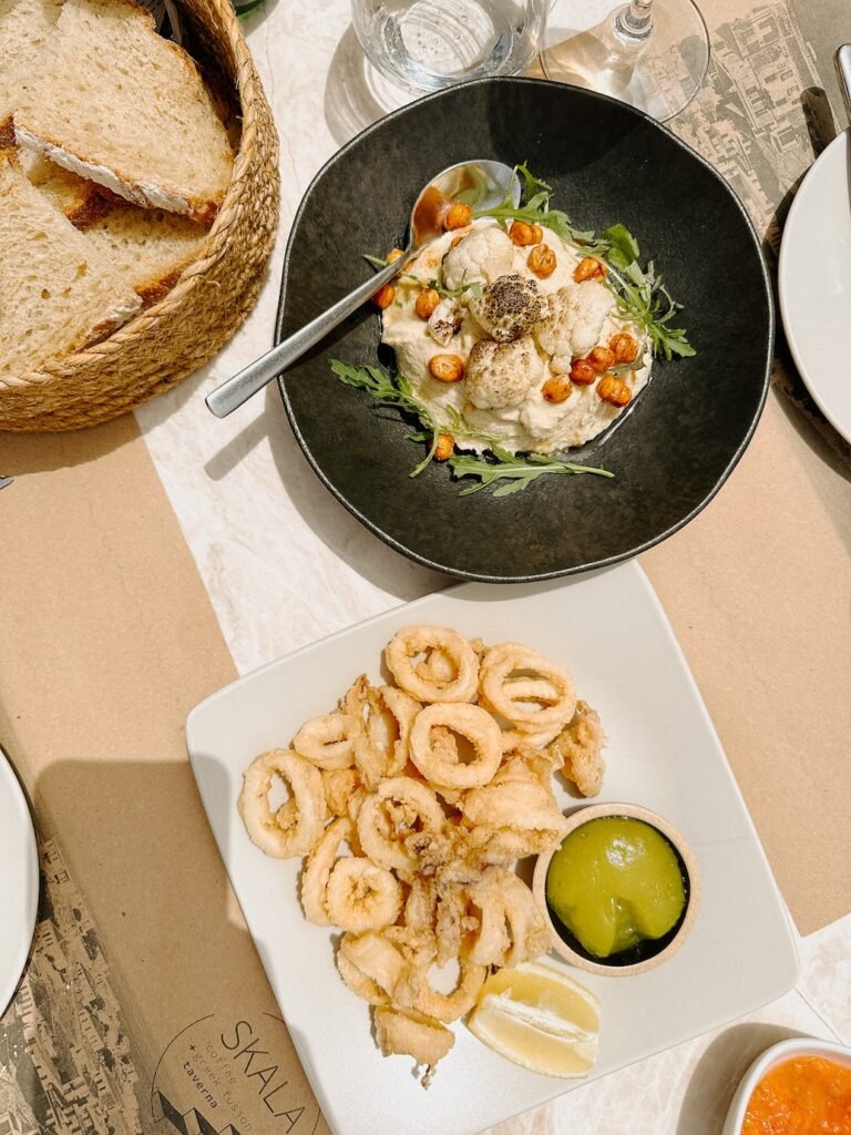 A delicious spread of Greek cuisine with fresh hummus, crispy calamari, and a glass of chilled white wine at a seaside taverna.