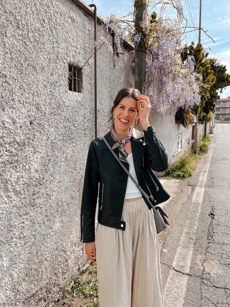 Lindsay standing in front of cascading purple wisteria, enjoying the beauty of springtime blooms in Italy