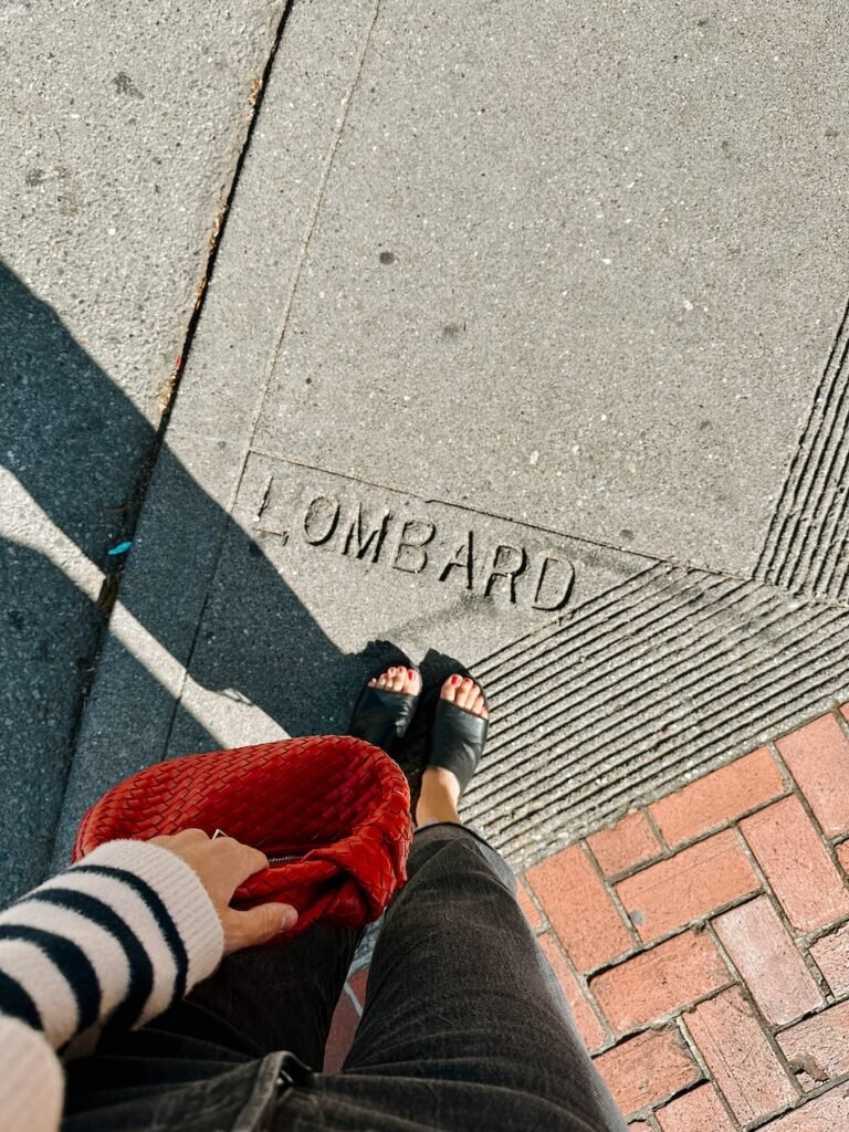 A personal moment standing on Lombard Street, holding a red purse, with "Lombard Street" engraved in the cement beneath my feet.