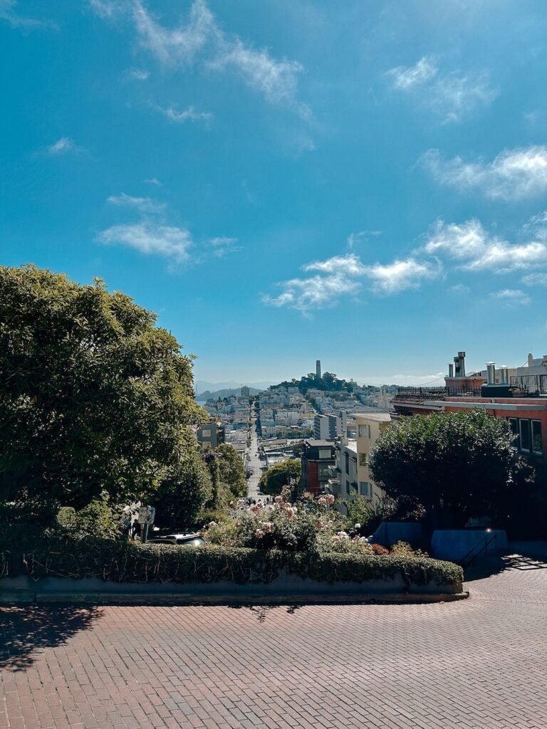The famous winding Lombard Street, lined with lush greenery and colorful flowers, with cars carefully making their way down the steep curves.
