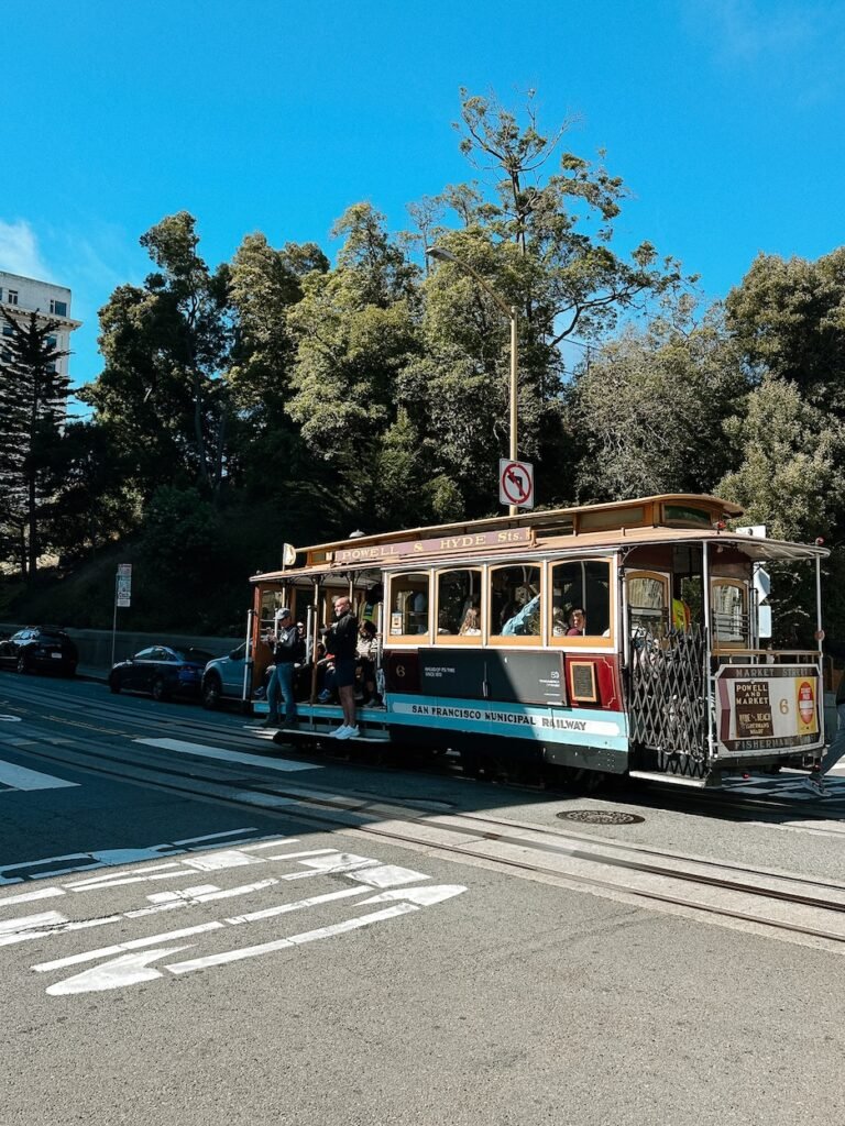 A classic San Francisco cable car, painted bright red with the Wells Fargo logo, traveling up a steep street. A must-see for first-time visitors!