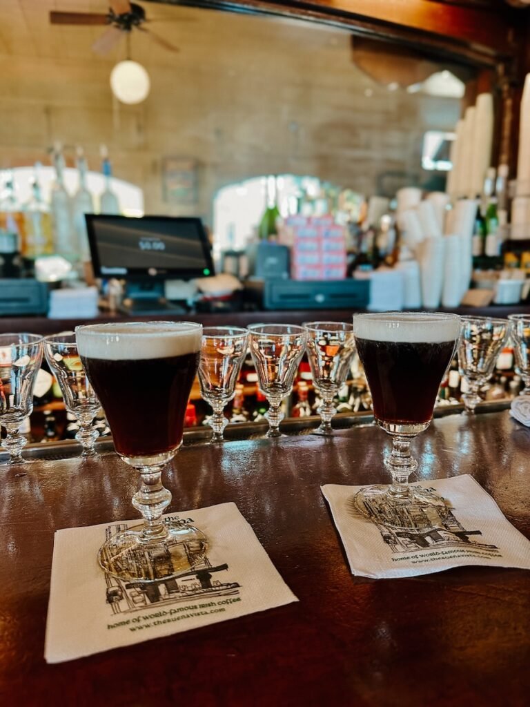 A cozy scene inside Buena Vista Café, featuring a classic Irish coffee with layers of rich coffee, whiskey, and cream in a glass mug.