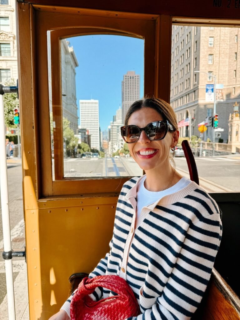 A classic San Francisco cable car in motion, with passengers hanging onto the sides as it climbs the city’s steep streets.