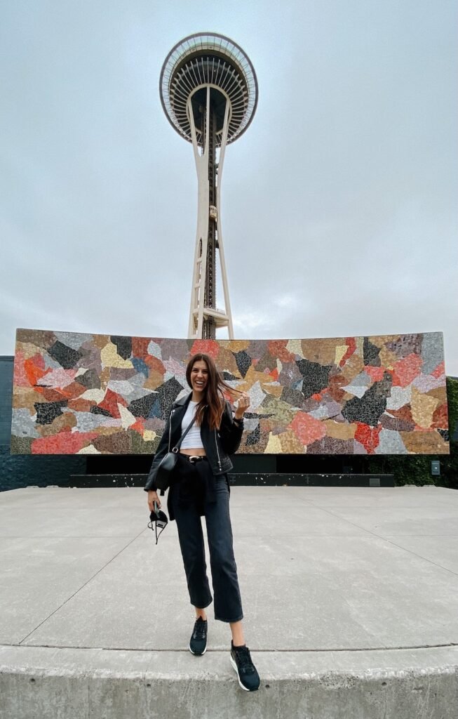 A traveler standing in front of the Seattle Space Needle, capturing the perfect tourist photo.